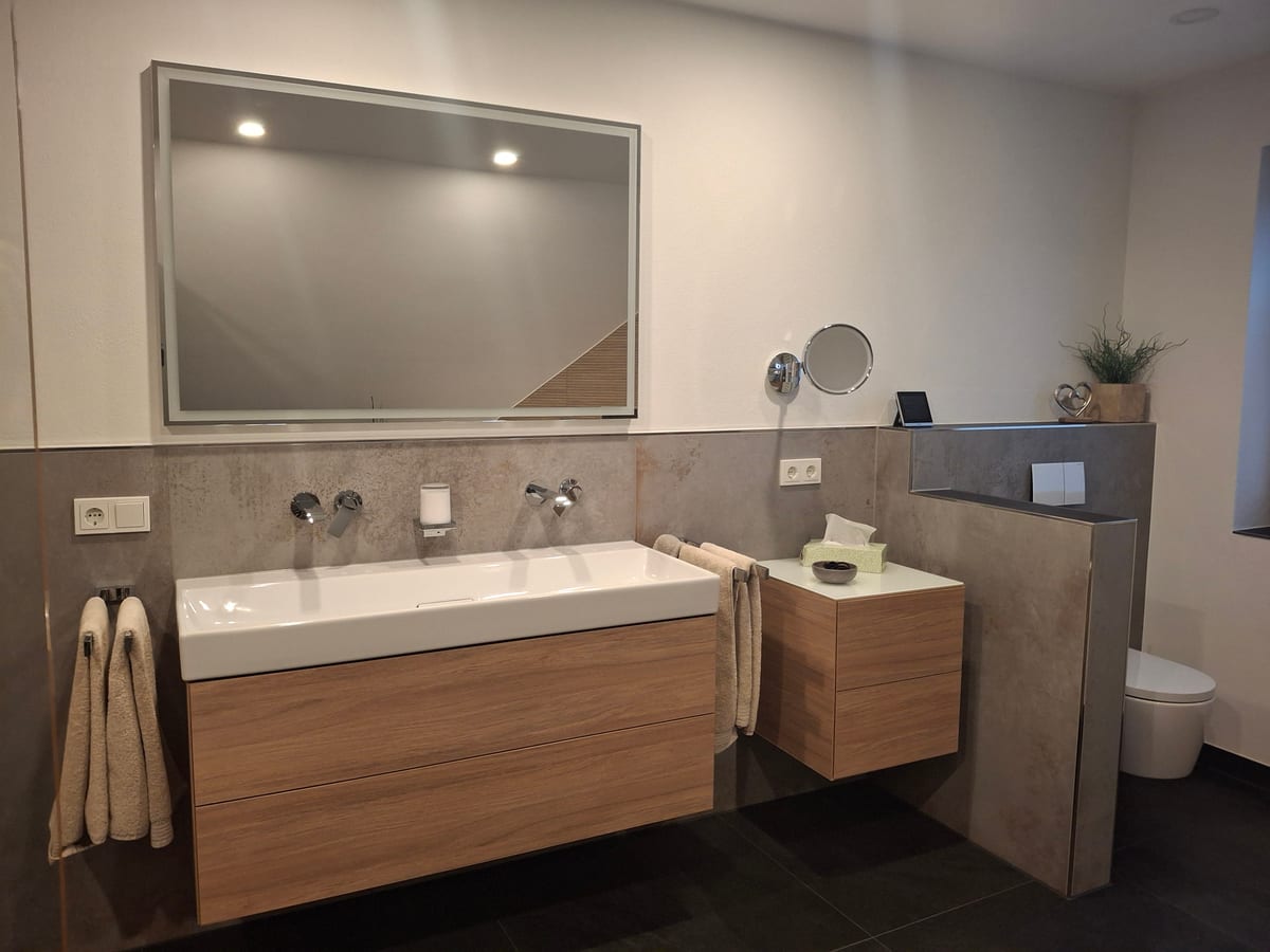 Modernes Badezimmer mit Doppelwaschtisch in Holzoptik, großem Spiegel, Wand-WC und gläserner bodengleicher Dusche, Komplettbadsanierung in Luxemburg